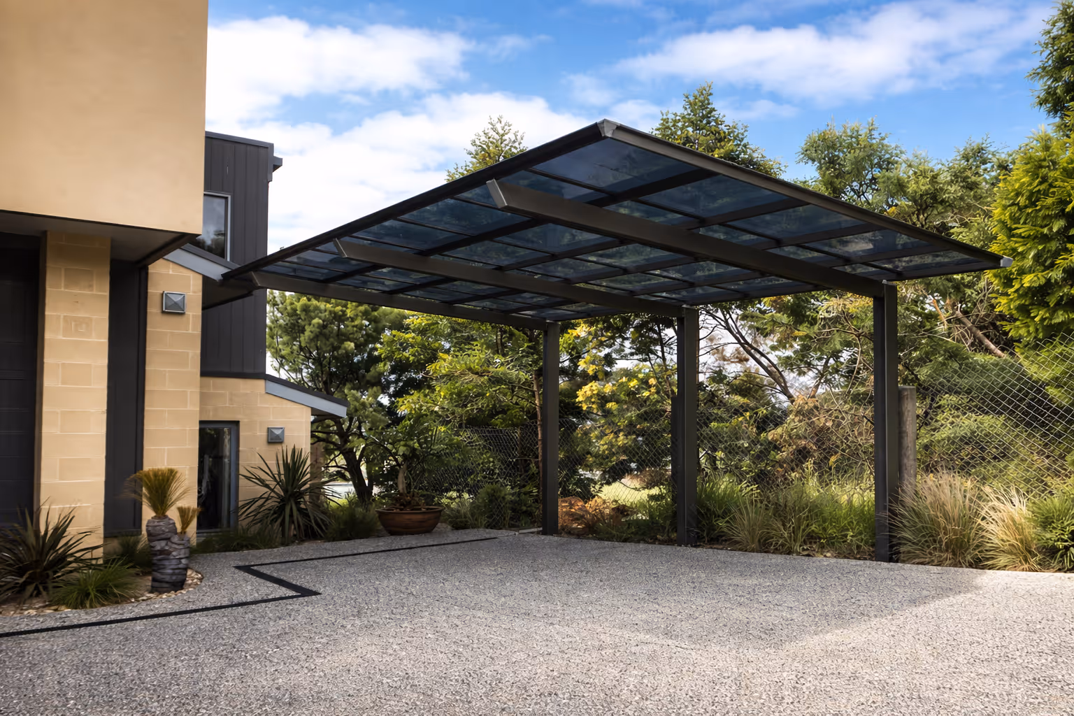 Modern carport with a transparent roof next to a beige and black house surrounded by greenery.